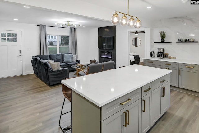 kitchen with gray cabinetry, a kitchen island, a breakfast bar, light wood-type flooring, and light countertops