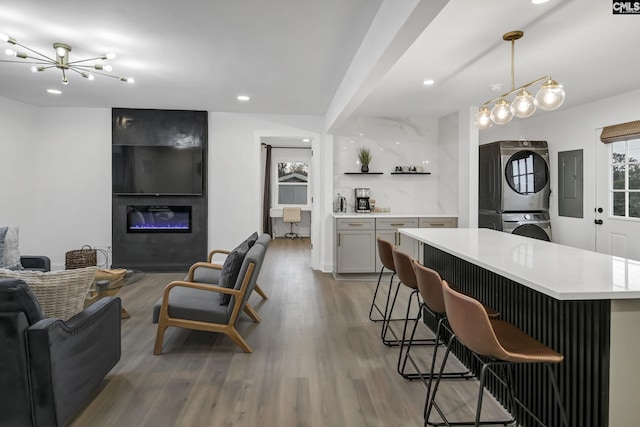 kitchen featuring stacked washer / dryer, a large fireplace, open floor plan, a breakfast bar, and wood finished floors