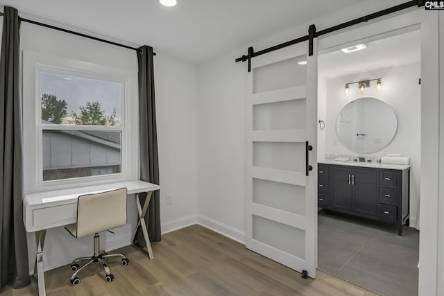 office space with built in features, a sink, wood finished floors, a barn door, and baseboards