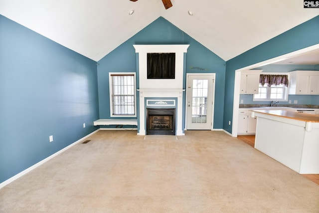 unfurnished living room with baseboards, ceiling fan, a fireplace with flush hearth, light colored carpet, and a sink