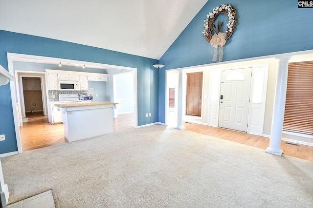 unfurnished living room with light carpet, high vaulted ceiling, and decorative columns