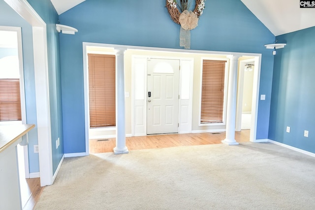 carpeted foyer featuring baseboards, ornate columns, and high vaulted ceiling