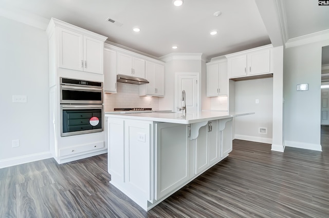 kitchen featuring visible vents, white cabinets, under cabinet range hood, double oven, and backsplash