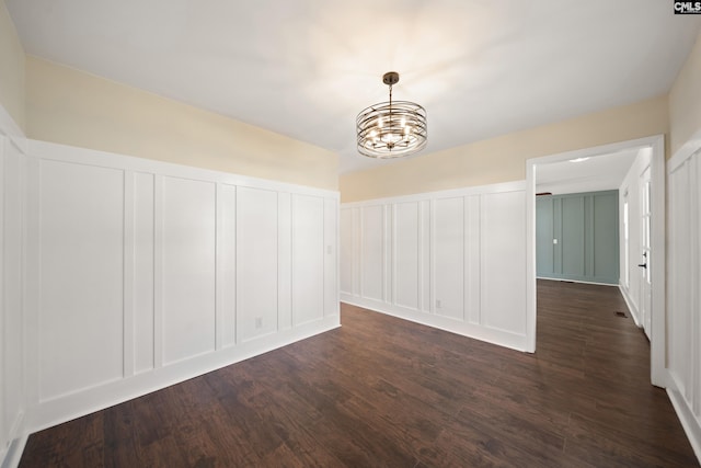 unfurnished room featuring a chandelier, a decorative wall, and dark wood-style flooring