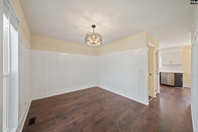 empty room with visible vents, a notable chandelier, dark wood finished floors, and a decorative wall