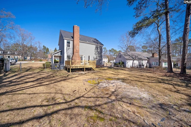 rear view of house featuring a wooden deck, a chimney, and fence