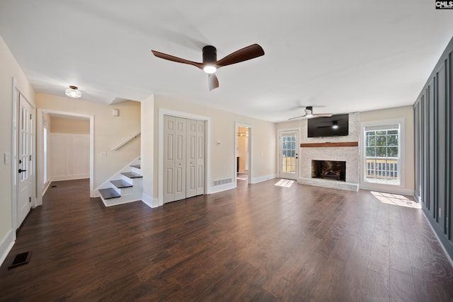 unfurnished living room featuring visible vents, a ceiling fan, dark wood-style floors, stairway, and a large fireplace