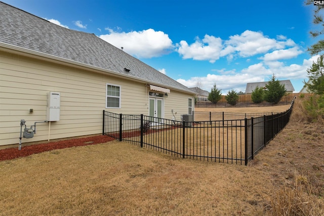 back of house featuring a lawn, central AC unit, a shingled roof, and fence