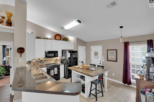 kitchen featuring visible vents, black appliances, a sink, dark countertops, and lofted ceiling