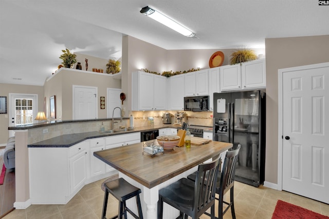 kitchen featuring a peninsula, a sink, black appliances, white cabinets, and butcher block counters