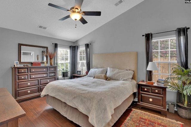 bedroom with a textured ceiling, lofted ceiling, visible vents, and dark wood-type flooring