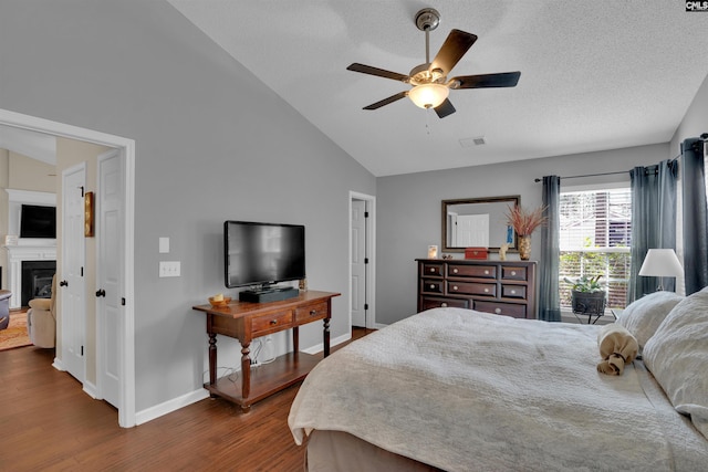 bedroom featuring dark wood-style floors, visible vents, baseboards, a fireplace, and vaulted ceiling