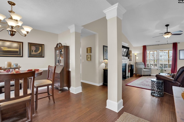 dining area featuring decorative columns, a glass covered fireplace, dark wood finished floors, and ceiling fan with notable chandelier