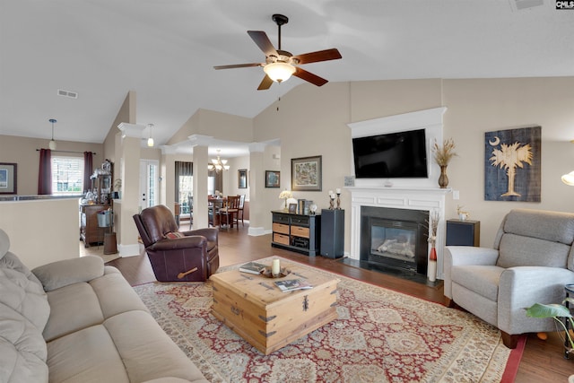 living room with wood finished floors, visible vents, lofted ceiling, a fireplace with flush hearth, and ceiling fan with notable chandelier