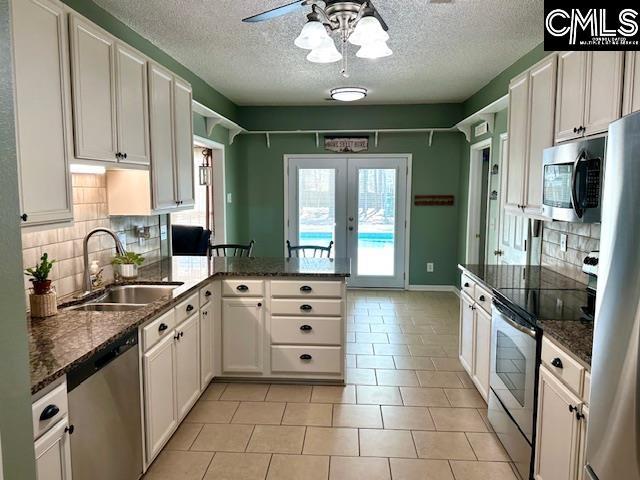 kitchen with appliances with stainless steel finishes, french doors, a peninsula, white cabinetry, and a sink