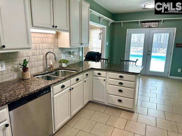 kitchen featuring a sink, dishwasher, a peninsula, and white cabinetry