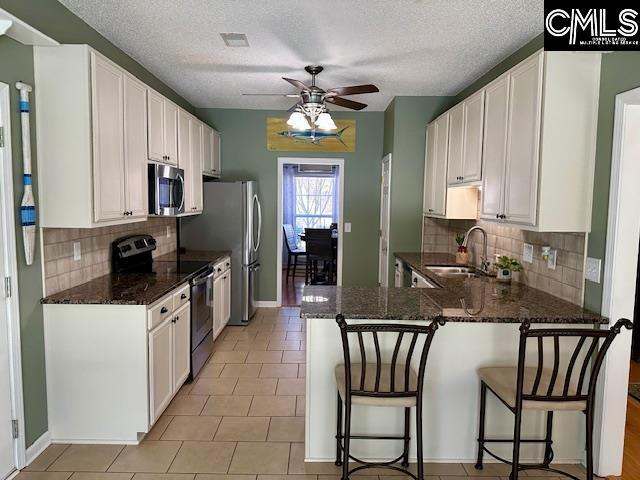 kitchen featuring appliances with stainless steel finishes, white cabinetry, a kitchen bar, and a sink