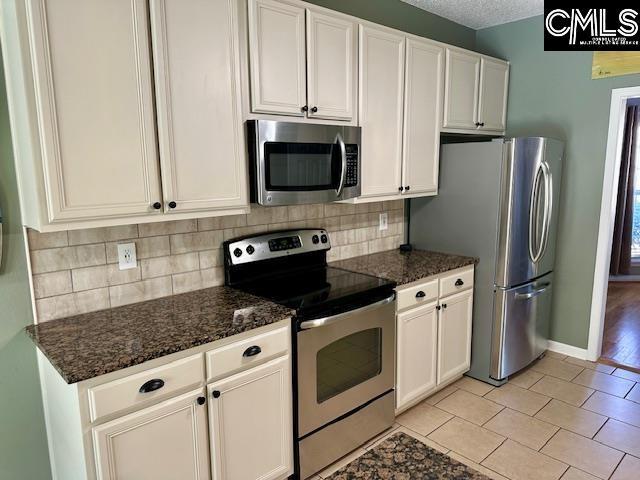 kitchen with backsplash, white cabinetry, baseboards, appliances with stainless steel finishes, and a textured ceiling