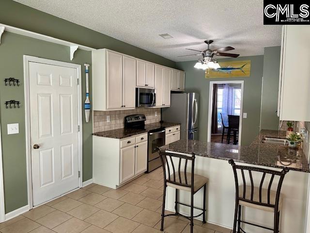 kitchen with tasteful backsplash, appliances with stainless steel finishes, white cabinetry, and a peninsula