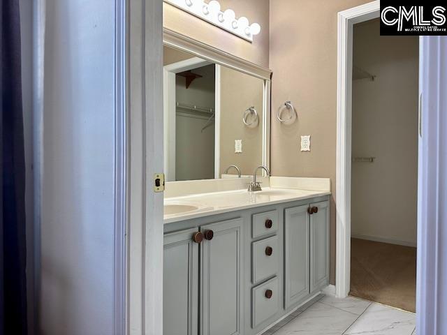 full bathroom featuring double vanity, a spacious closet, marble finish floor, and a sink