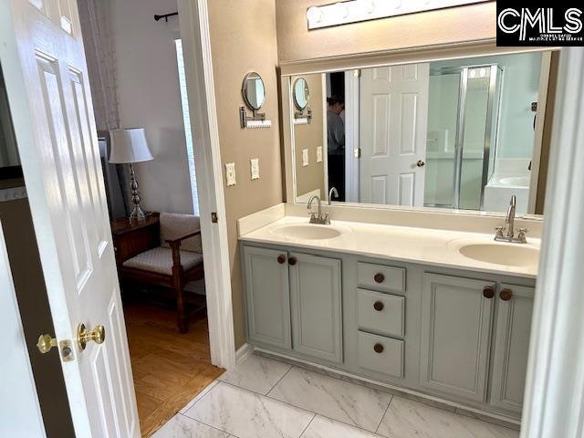 full bath featuring double vanity, marble finish floor, and a sink