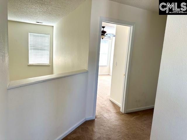 hallway featuring baseboards, a textured ceiling, and carpet