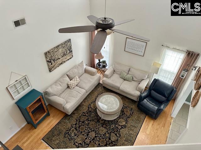 living area with a towering ceiling, visible vents, wood finished floors, and a ceiling fan