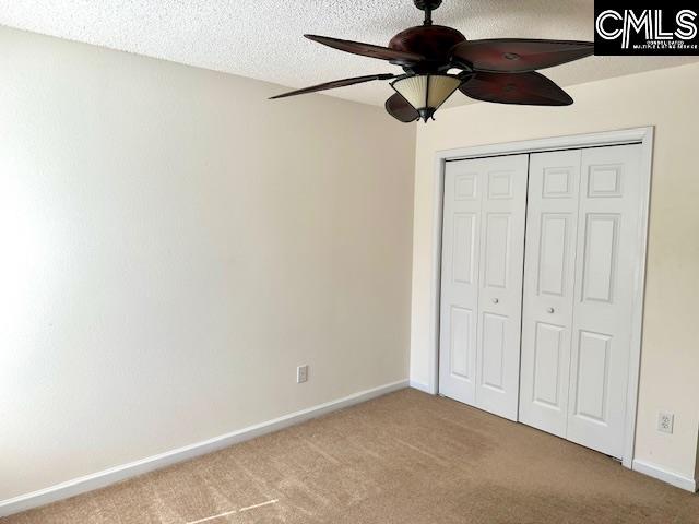 unfurnished bedroom with baseboards, carpet flooring, a closet, a textured ceiling, and a ceiling fan