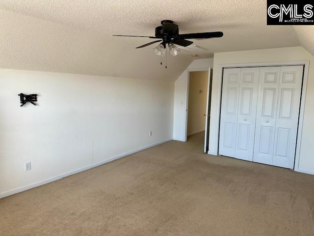 unfurnished bedroom featuring a textured ceiling, a closet, carpet flooring, lofted ceiling, and ceiling fan