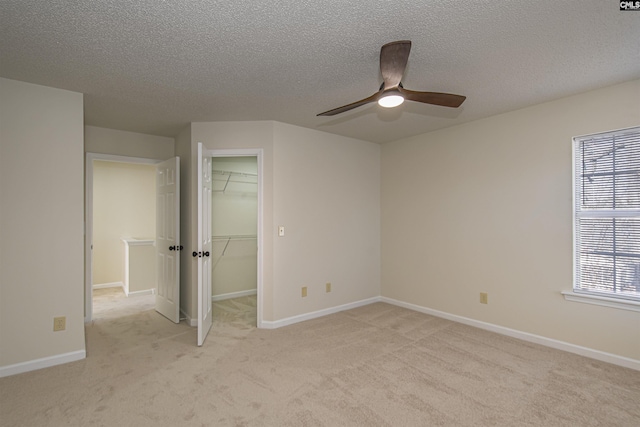 unfurnished bedroom with a spacious closet, light colored carpet, baseboards, and ceiling fan