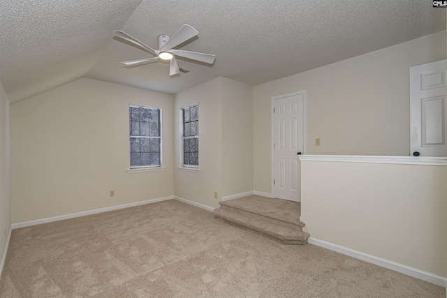 carpeted spare room featuring a textured ceiling, vaulted ceiling, baseboards, and ceiling fan