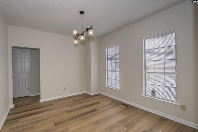 spare room featuring a chandelier, a textured ceiling, light wood-type flooring, and baseboards