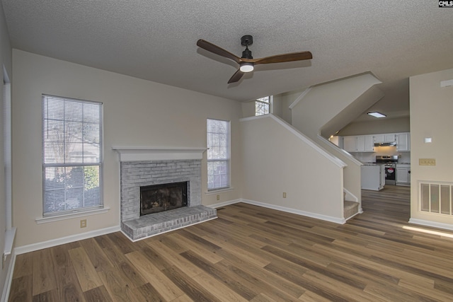 unfurnished living room featuring visible vents, dark wood-type flooring, baseboards, a brick fireplace, and stairs