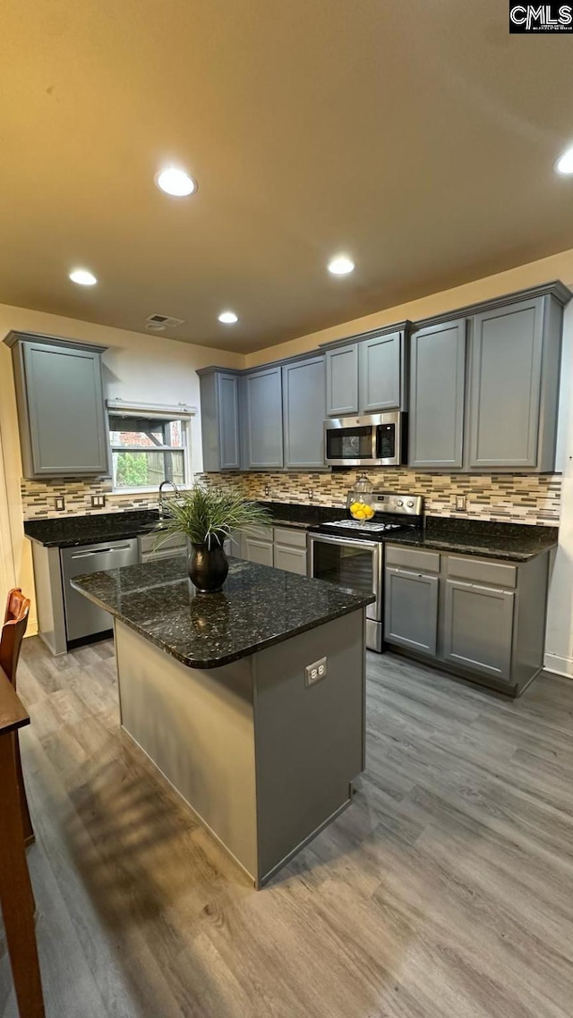 kitchen featuring wood finished floors, a kitchen island, dark stone counters, stainless steel appliances, and tasteful backsplash