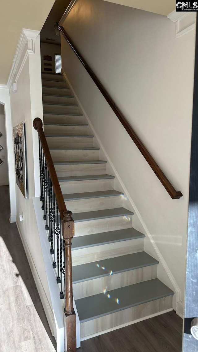 stairway with wood finished floors and ornamental molding