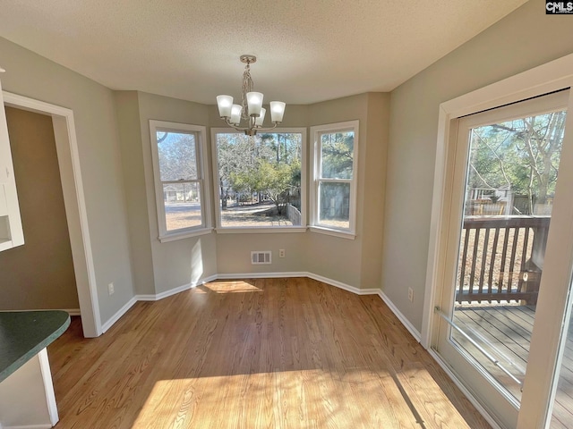 unfurnished dining area with visible vents, baseboards, an inviting chandelier, wood finished floors, and a textured ceiling