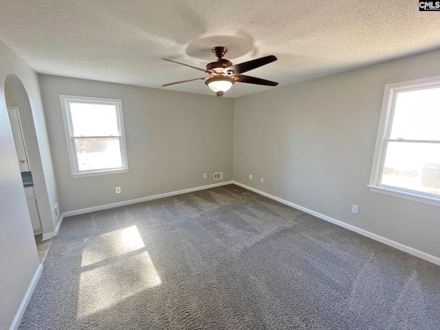 empty room featuring a ceiling fan, visible vents, baseboards, arched walkways, and carpet flooring