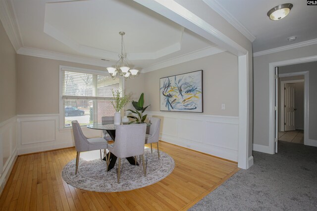 dining area featuring ornamental molding, hardwood / wood-style floors, wainscoting, a notable chandelier, and a raised ceiling