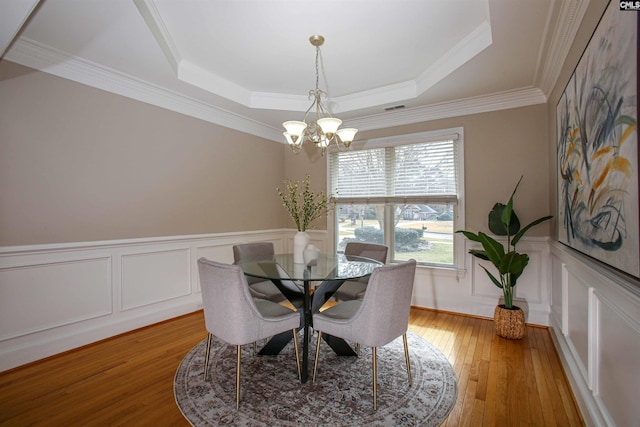 dining room with a wainscoted wall, visible vents, an inviting chandelier, a tray ceiling, and light wood-style floors