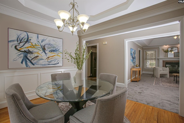 dining area with a notable chandelier, ornamental molding, a decorative wall, light wood finished floors, and a brick fireplace