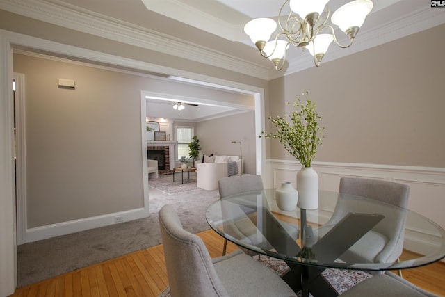 dining area with a chandelier, ornamental molding, wainscoting, a fireplace, and wood finished floors