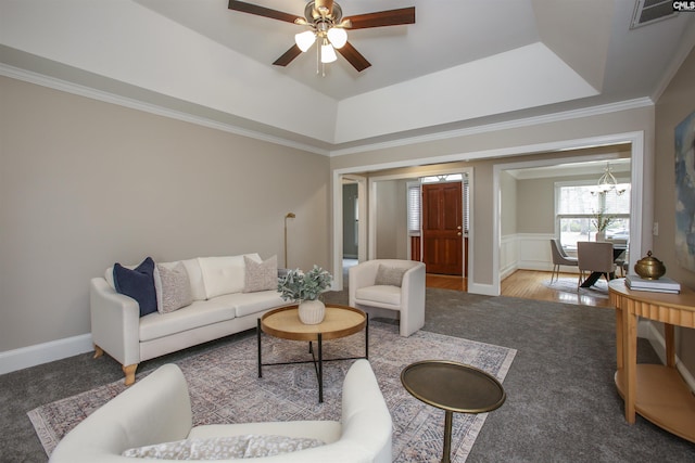 living room with baseboards, visible vents, ornamental molding, a raised ceiling, and ceiling fan with notable chandelier