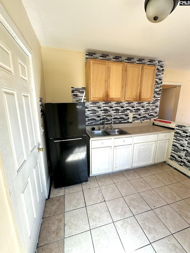 kitchen featuring a sink, tasteful backsplash, freestanding refrigerator, light countertops, and light tile patterned floors