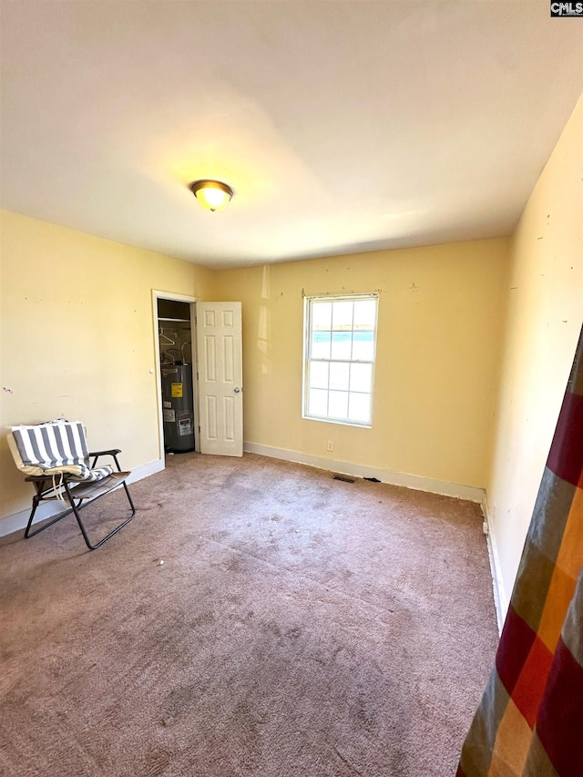 empty room with visible vents, carpet, baseboards, and electric water heater