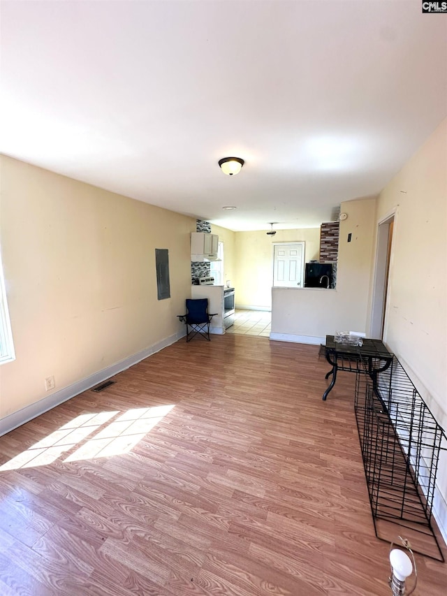 unfurnished living room featuring electric panel, visible vents, baseboards, and wood finished floors