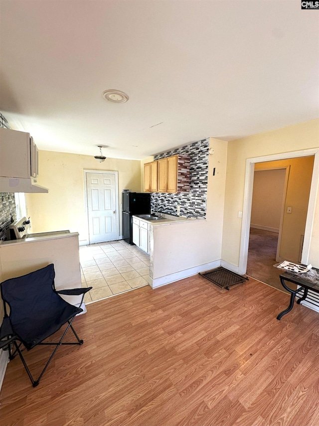 kitchen with tasteful backsplash, freestanding refrigerator, light wood-type flooring, and under cabinet range hood