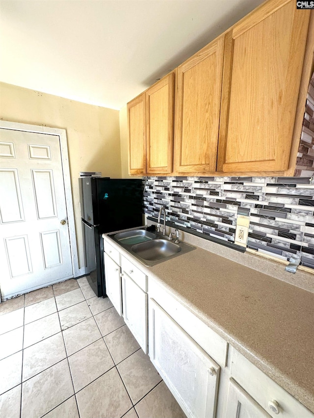 kitchen with a sink, freestanding refrigerator, light countertops, light tile patterned floors, and decorative backsplash