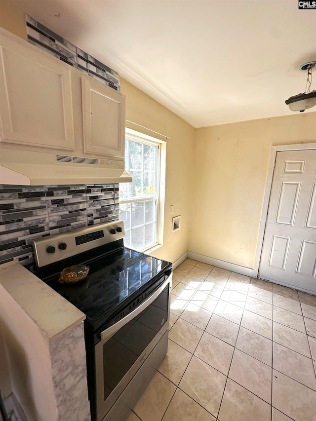 kitchen with tasteful backsplash, baseboards, under cabinet range hood, light tile patterned floors, and electric range