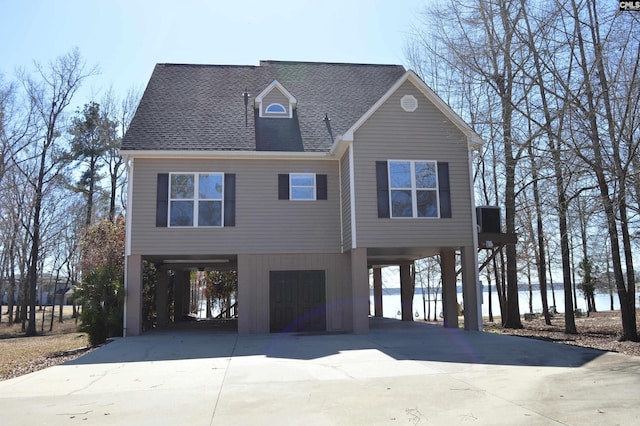 raised beach house featuring a carport, roof with shingles, and driveway