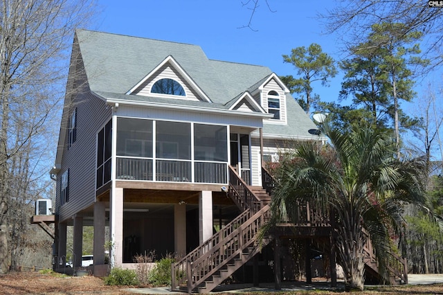 rear view of house featuring stairway, central AC unit, a shingled roof, and a sunroom